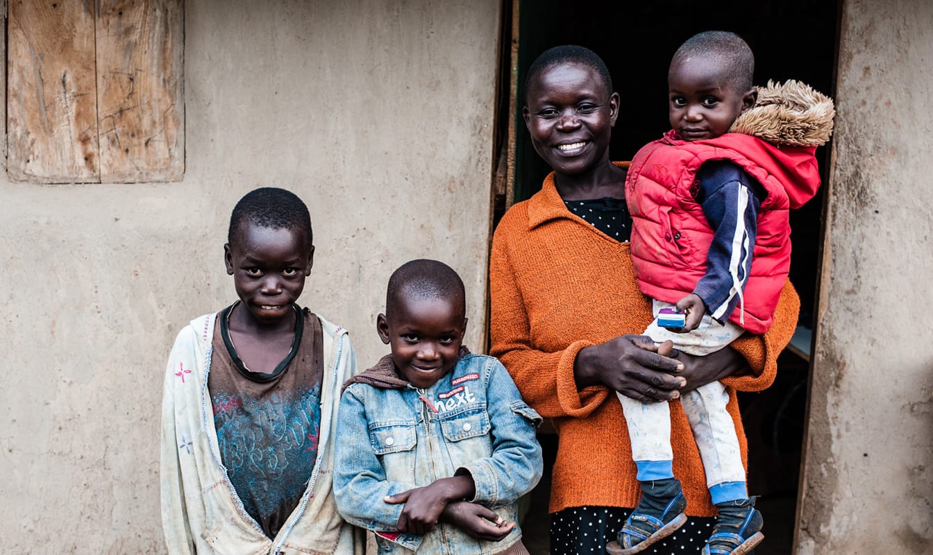 A mother and three children, recipients of GiveDirectly funding, smile in front of their home.