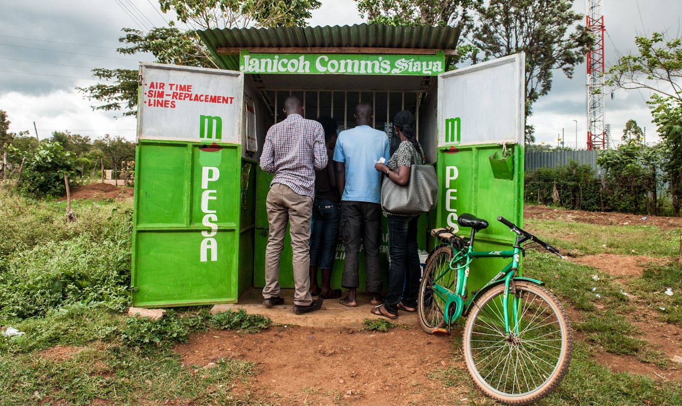 Three people at a mobile device maintenance kiosk, where their phone-based credit can be exchanged for cash.