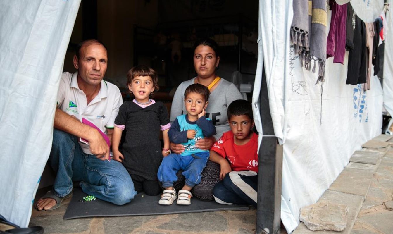 Field workers pose with three refugee children in the doorway of a temporary shelter.