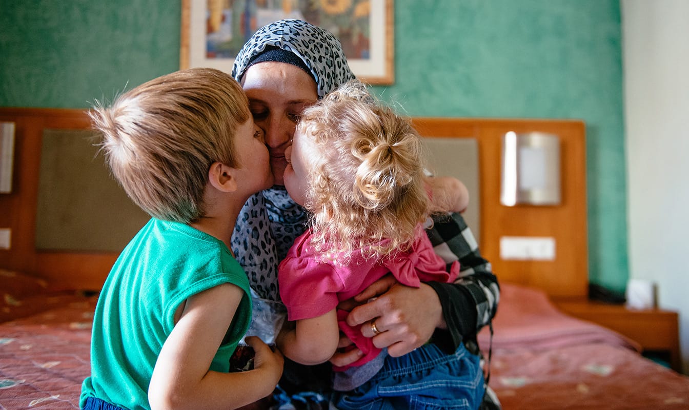 A Mercy Corps field worker embraces two refugee children.