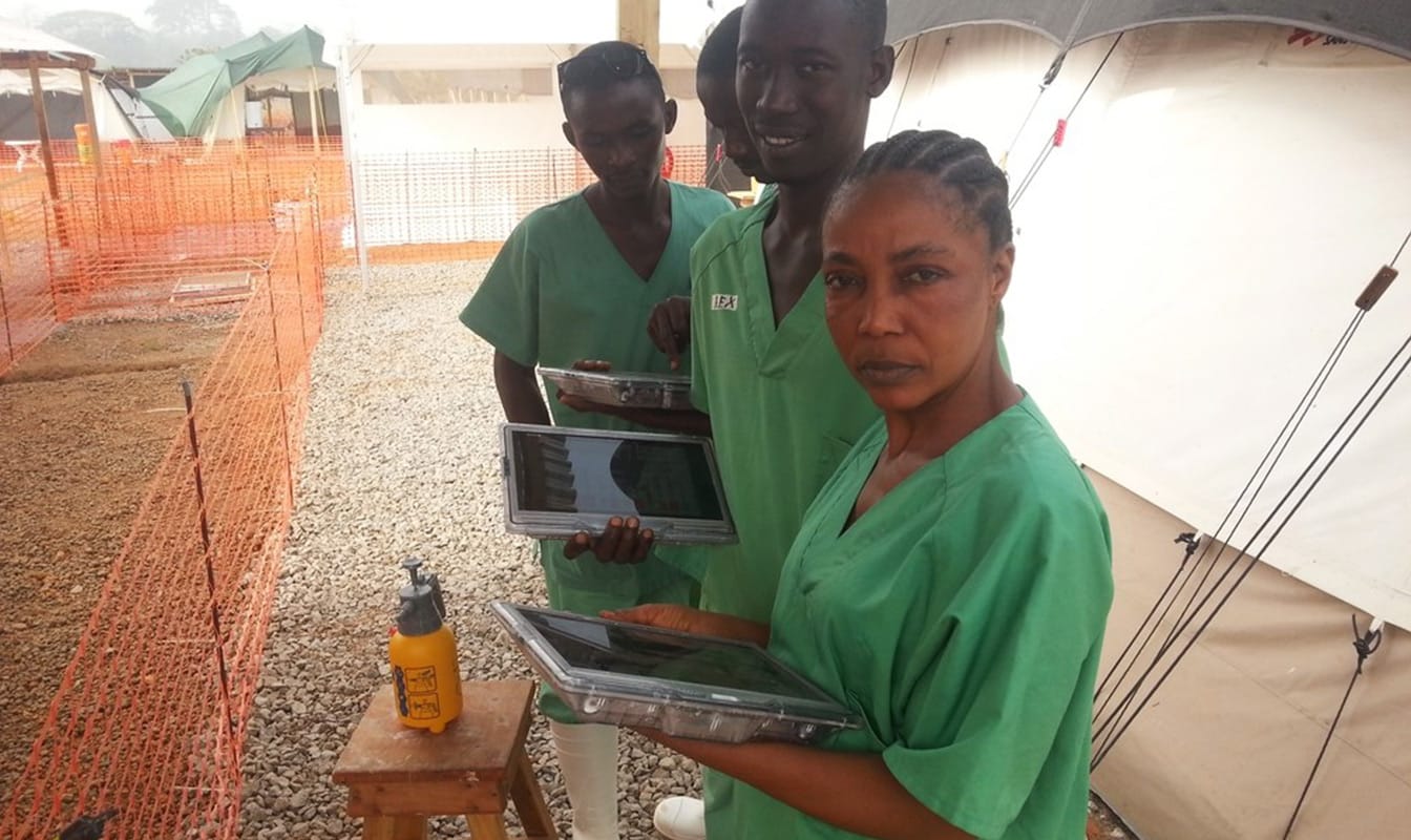 Four MSF field workers look into the camera while using their tablets to access the Project Buendia app.