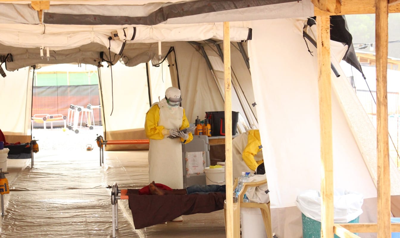 An MSF field worker in a medical tent tends to a sick patient, while another uses a tablet to access Project Buendia.
