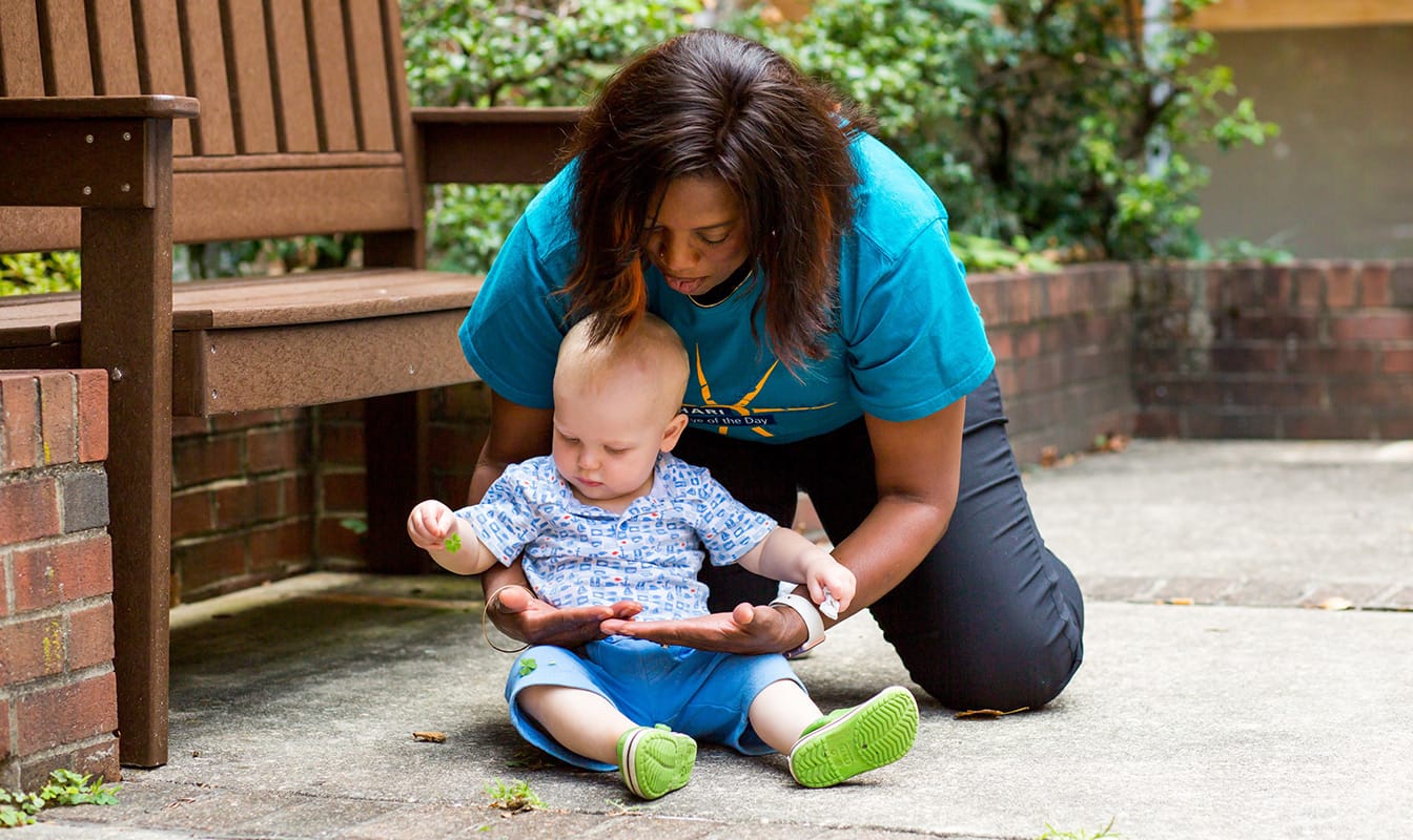 An NDWA-affiliated nanny entertains an infant near a park bench