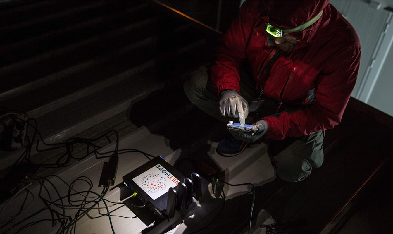 A NetHope field worker wears a headlamp while installing a device-charging station.