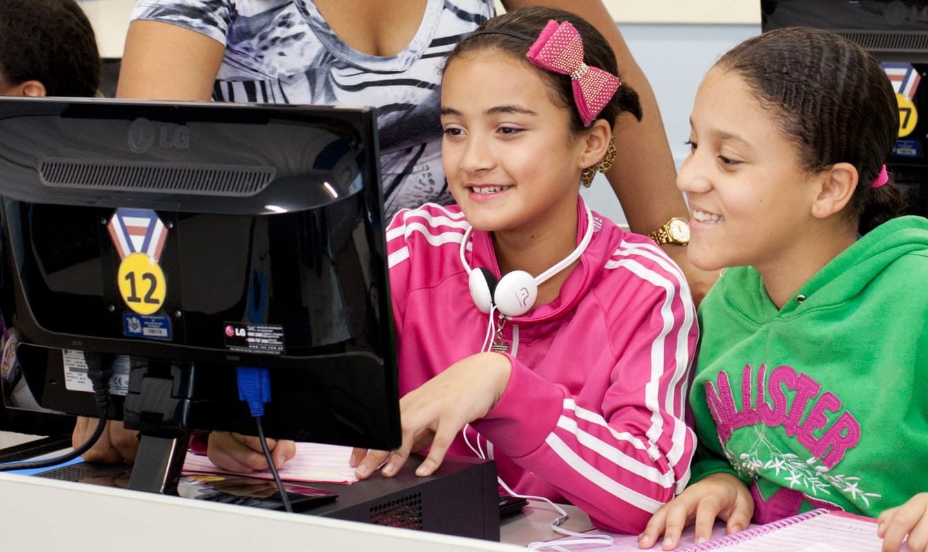 Two Brazilian youths and an instructor look at a computer during a digital lesson.