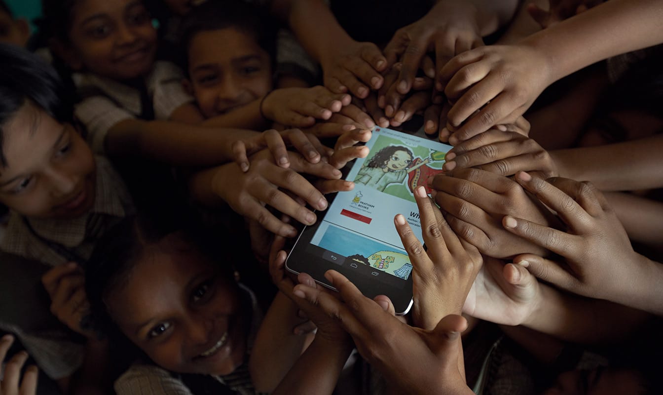 Un groupe d'élèves, le sourire aux lèvres, tente d'attraper une tablette sur laquelle une histoire traduite est affichée.